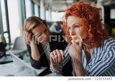 Two female colleagues analyzing project documents in modern office. Two female colleagues analyzing project documents in modern office. 129755457