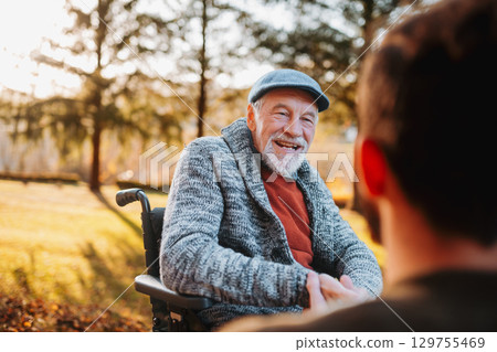 Man talking with his grandad in wheelchair during walk in fall nature. Man talking with his grandad in wheelchair during walk in fall nature. 129755469