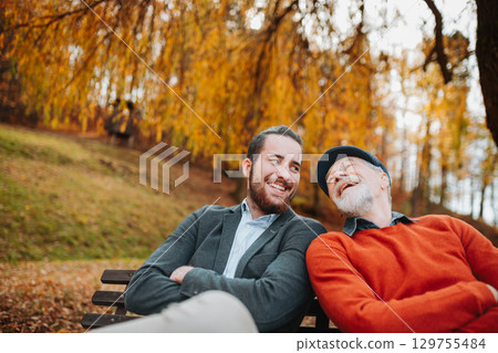 Grandad and grandson sitting on bench in park and talking. 129755484