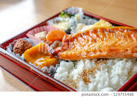 A Japanese-style bento box with grilled salmon as the main dish, rice, simmered dishes, and tamagoyaki (rolled egg). A Japanese-style bento box with grilled salmon as the main dish, rice, simmered dishes, and tamagoyaki (rolled egg). 129755486