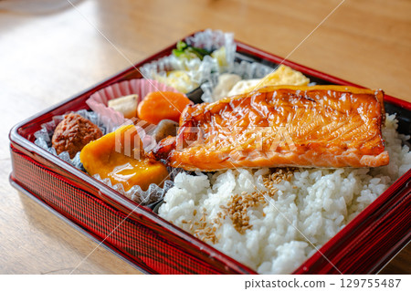 A Japanese-style bento box with grilled salmon as the main dish, rice, simmered dishes, and tamagoyaki (rolled egg). 129755487