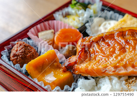 A Japanese-style bento box with grilled salmon as the main dish, rice, simmered dishes, and tamagoyaki (rolled egg). 129755490