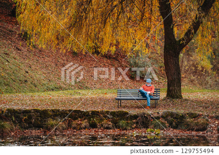 Pensive older man sitting on bench by lake and thinking. Pensive older man sitting on bench by lake and thinking. 129755494