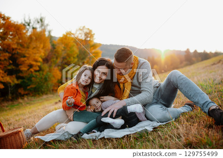 Parents with young children sitting outdoors in autumn light. Parents with young children sitting outdoors in autumn light. 129755499