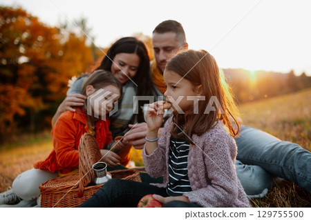 Parents with young children sitting outdoors in autumn light. Parents with young children sitting outdoors in autumn light. 129755500