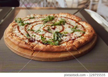 Pizza with arugula on a wooden plate on grey background in summer terrace Pizza with arugula on a wooden plate on grey background in summer terrace 129755535