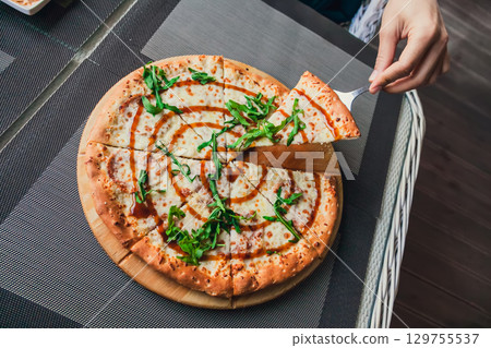 Man takes a slice of pizza from a whole on a gray background in a street cafe, top view Man takes a slice of pizza from a whole on a gray background in a street cafe, top view 129755537