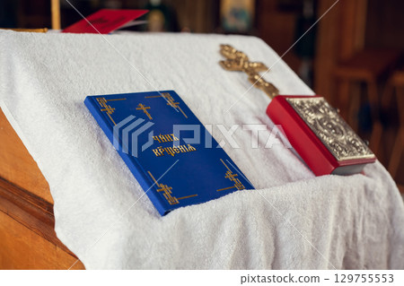 The sacrament of baptism in the Orthodox Church. Prayer books and a crucifix on the table. Inscription on the book: the rite of baptism. 129755553