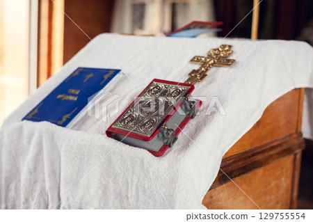 The sacrament of baptism in the Orthodox Church. Prayer books and a crucifix on the table. Inscription on the book: the rite of baptism. 129755554