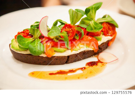 Vibrant open-faced sandwich topped with fresh vegetables served on a white plate 129755576