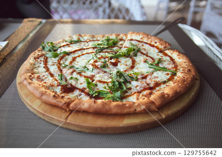 Pizza with arugula on a wooden plate on grey background in summer terrace 129755642