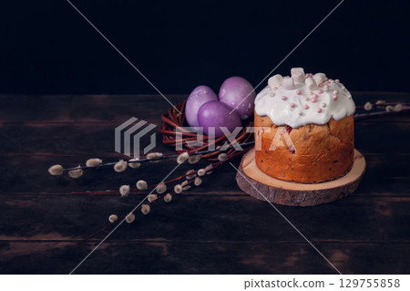 Easter cakes on a dark background, decorated with marshmallows and painted Easter eggs in a wicker nest 129755858