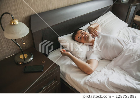A middle-aged man in bed in his bedroom wakes up in the morning with a smile on his face. The concept of healthy sleep 129755882