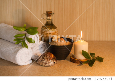 Spa, beauty and wellness background. Towel, cosmetic massage oil, leaf, sea salt with shells and candle 129755971