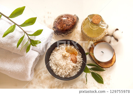 Spa, beauty and wellness. Towel, cosmetic massage oil, leaf, sea salt with shells and candle. Top view, flat lay on white backgroun 129755978