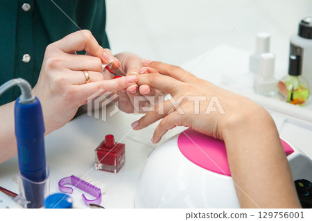 Gel polish design. Female master in the salon is painting with brush on the hands of the client. Beauty industry, creativity concept 129756001