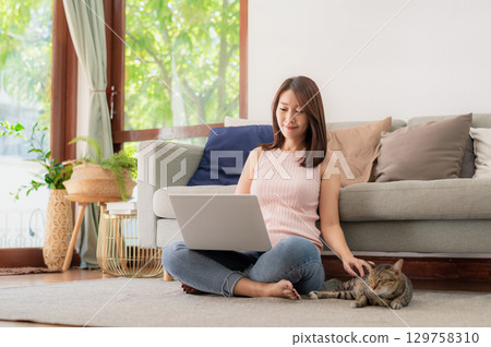 Woman using laptop and playing with cat 129758310