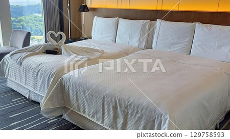 A luxurious bedroom with a bright window and heart-shaped towel art 129758593