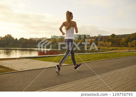 Female young runner jogging alone in city park. Healthy sporty fitness woman running outdoors. 129758793