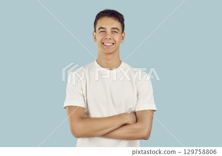 Portrait of happy, cheerful young man or teenage boy with folded arms on blue background Portrait of happy, cheerful young man or teenage boy with folded arms on blue background 129758806