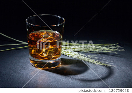 glass of amber whiskey and ears of rye on a black stone table. 129759028