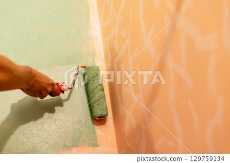 Hand of a person applying green paint with roller on wall, painting process in a home improvement project with textured background Hand of a person applying green paint with roller on wall, painting process in a home improvement project with textured background 129759134