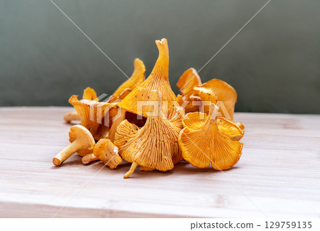 Vibrant yellow chanterelle mushrooms arranged artistically on wooden surface, showcasing their unique shapes and textures, culinary or nature themed projects, Cantharellus cibarius, girolle 129759135