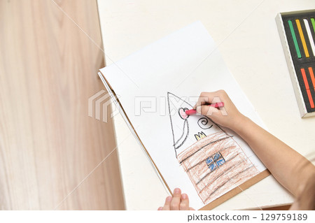 Child drawing house with crayons on white paper at home desk Child drawing house with crayons on white paper at home desk 129759189