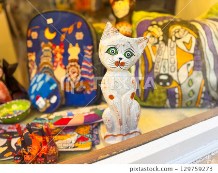 A shop window with colorful souvenirs and wooden cat figurine placed in display. Creativity, culture, art and decoration in handmade product and local market style. A shop window with colorful souvenirs and wooden cat figurine placed in display. Creativity, culture, art and decoration in handmade product and local market style. 129759273