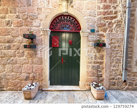 A green wooden door with red mailbox and arched stone frame on a rustic wall. Architecture, tradition, entrance and residential identity in urban street facade. A green wooden door with red mailbox and arched stone frame on a rustic wall. Architecture, tradition, entrance and residential identity in urban street facade. 129759274