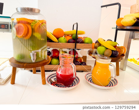 A buffet table with pitchers of fresh juices, infused water and assorted fruits in wooden trays. Freshness, nutrition, vitamins and hospitality in hotel breakfast dining. A buffet table with pitchers of fresh juices, infused water and assorted fruits in wooden trays. Freshness, nutrition, vitamins and hospitality in hotel breakfast dining. 129759294
