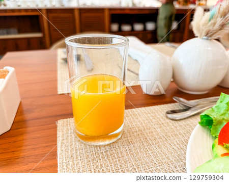 A glass of orange juice on a breakfast table in a hotel restaurant. Health, vitamin, refreshment and morning nutrition in dining atmosphere and lifestyle setting. 129759304