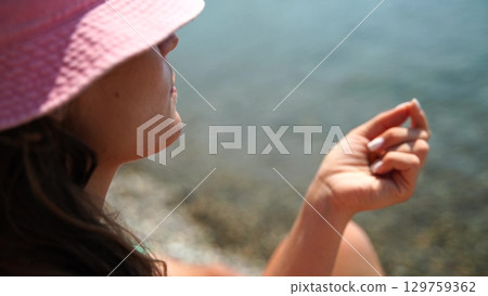 Seashore Woman Summer: Woman examines seashell sitting seaside on summer day, enjoying tranquility, sunbathing. Seashore Woman Summer: Woman examines seashell sitting seaside on summer day, enjoying tranquility, sunbathing. 129759362