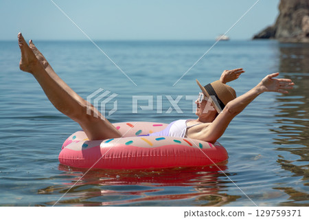 Woman floating sea, relaxing summer vacation on an inflatable donut ring in clear blue water. 129759371