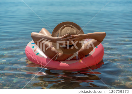 Woman floating water, enjoying peaceful summer vacation on an inflatable ring in clear sea with copy space. 129759373