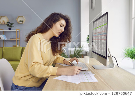 Female analyst checking spreadsheet on computer and doing paperwork Female analyst checking spreadsheet on computer and doing paperwork 129760647