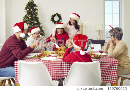 Christmas Thanksgiving dinner with turkey in big family aitting at table in Xmas interior at home. 129760653