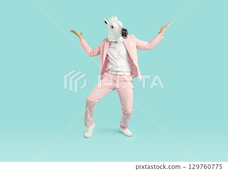 Funny man wearing bright pink suit in animal head horse mask having fun on studio blue background. 129760775