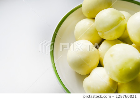 Ripe yellow plum in a green bowl. Juicy fruit on a white background. Ripe plums in drops of water. 129760821
