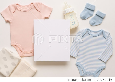 Flat lay of baby clothes and accessories with blank square card in center. Pink bodysuit, blue striped bodysuit, socks, baby bottle and blankets. newborn essentials, baby shower, gift set mockup 129760916