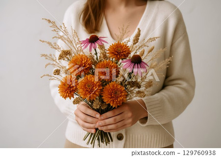Woman holding autumn bouquet with orange and purple flowers in hands capturing the beauty of fall season. concept of floral arrangement, seasonal decor, nature's elegance 129760938