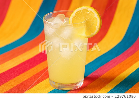 Refreshing lemonade with ice in a glass on a vibrant striped background. concept of summer refreshment, chilled drink, bright colors. Refreshing lemonade with ice in a glass on a vibrant striped background. concept of summer refreshment, chilled drink, bright colors. 129761086