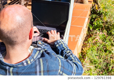 Smiling man working on laptop in hammock 129761398