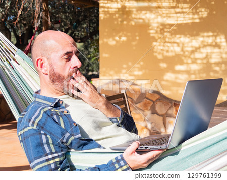 Shocked man looking at laptop in hammock Shocked man looking at laptop in hammock 129761399