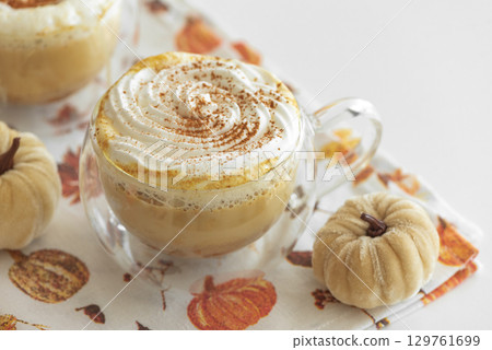 Cozy pumpkin latte with whipped cream and spices, surrounded by autumn decor. Cozy pumpkin latte with whipped cream and spices, surrounded by autumn decor. 129761699