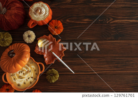 Autumnal lunch with pumpkin soup in a pumpkin-shaped bowl, pumpkin latte, croutons and festive decor on dark wooden table. Top view. Copy space 129761701