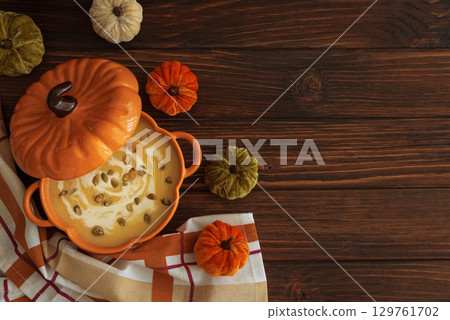 Autumnal lunch with pumpkin soup in a pumpkin-shaped bowl, croutons and festive decor on dark wooden table. Top view 129761702