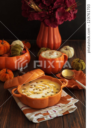 Autumnal lunch with pumpkin soup in a pumpkin-shaped bowl, pumpkin latte, croutons and festive decor on dark wooden table 129761703