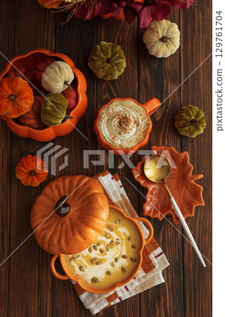 Autumnal lunch with pumpkin soup in a pumpkin-shaped bowl, pumpkin latte, croutons and festive decor on dark wooden table. Top view 129761704
