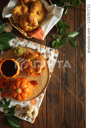 Autumnal tea set with pumpkin-shaped teapot and mug, and a baked bun on a wooden table. Top view. Copy space 129761711